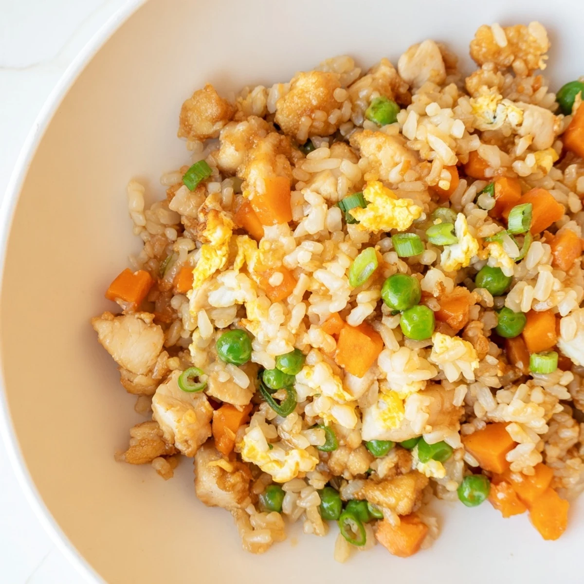 Steam rises from a skillet of freshly made Chicken Fried Rice with Peas and Carrots, showcasing scrambled eggs, diced chicken, and crisp vegetables for a satisfying, aromatic meal.