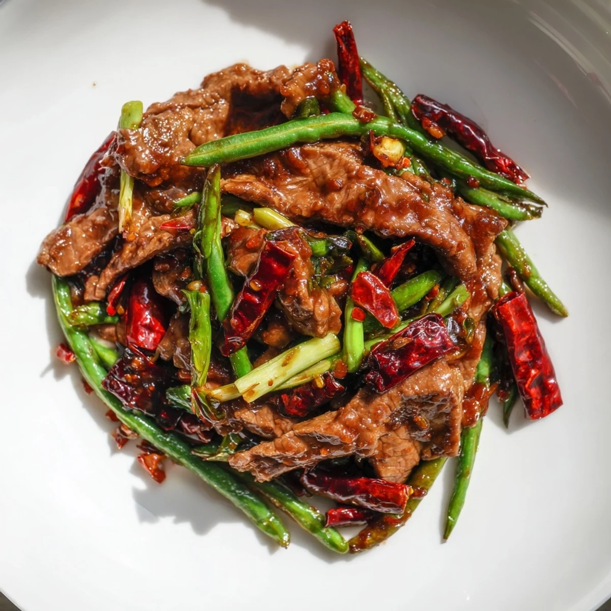 A steaming bowl of Spicy Szechuan Green Beans with Beef is served alongside fluffy white jasmine rice, garnished with sliced scallions and dried red chilies.