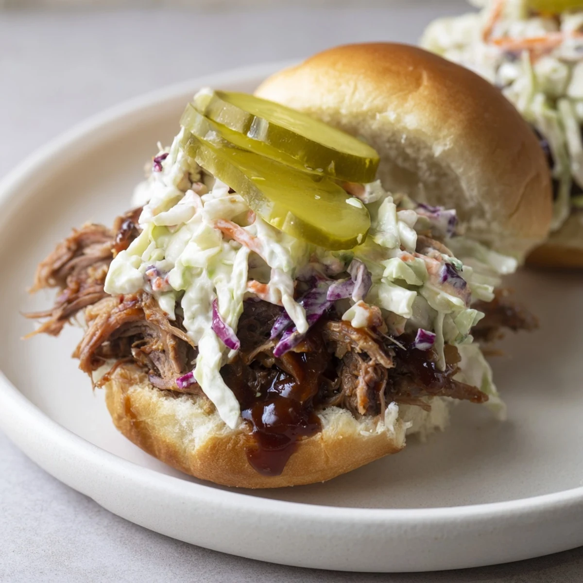 A close-up of beef brisket sliders with creamy coleslaw and tangy dill pickles on soft buns, drizzled with barbecue sauce.  