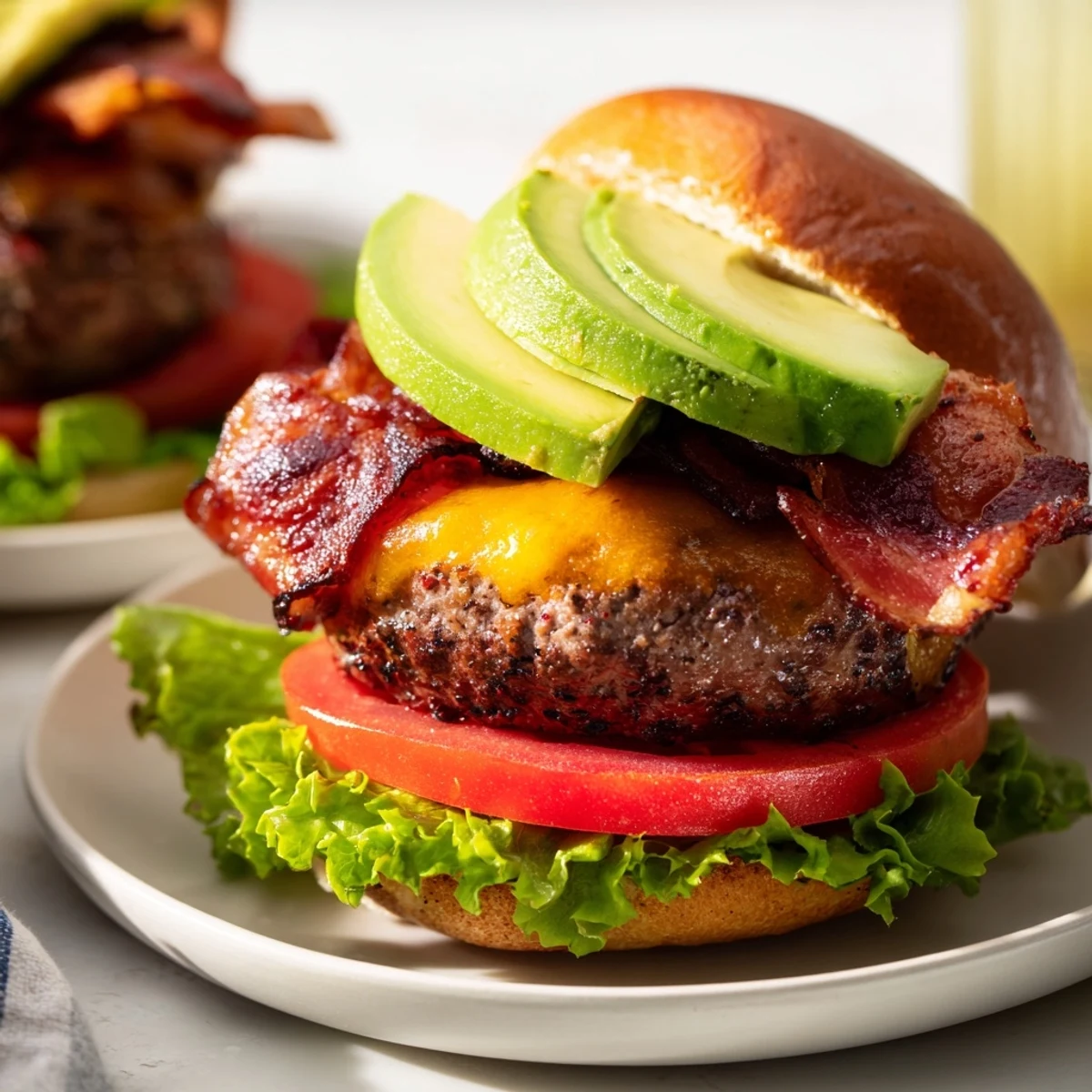 Juicy grilled beef burger with melted cheddar, crispy bacon, and fresh avocado slices on a toasted bun, served with lettuce and tomato.