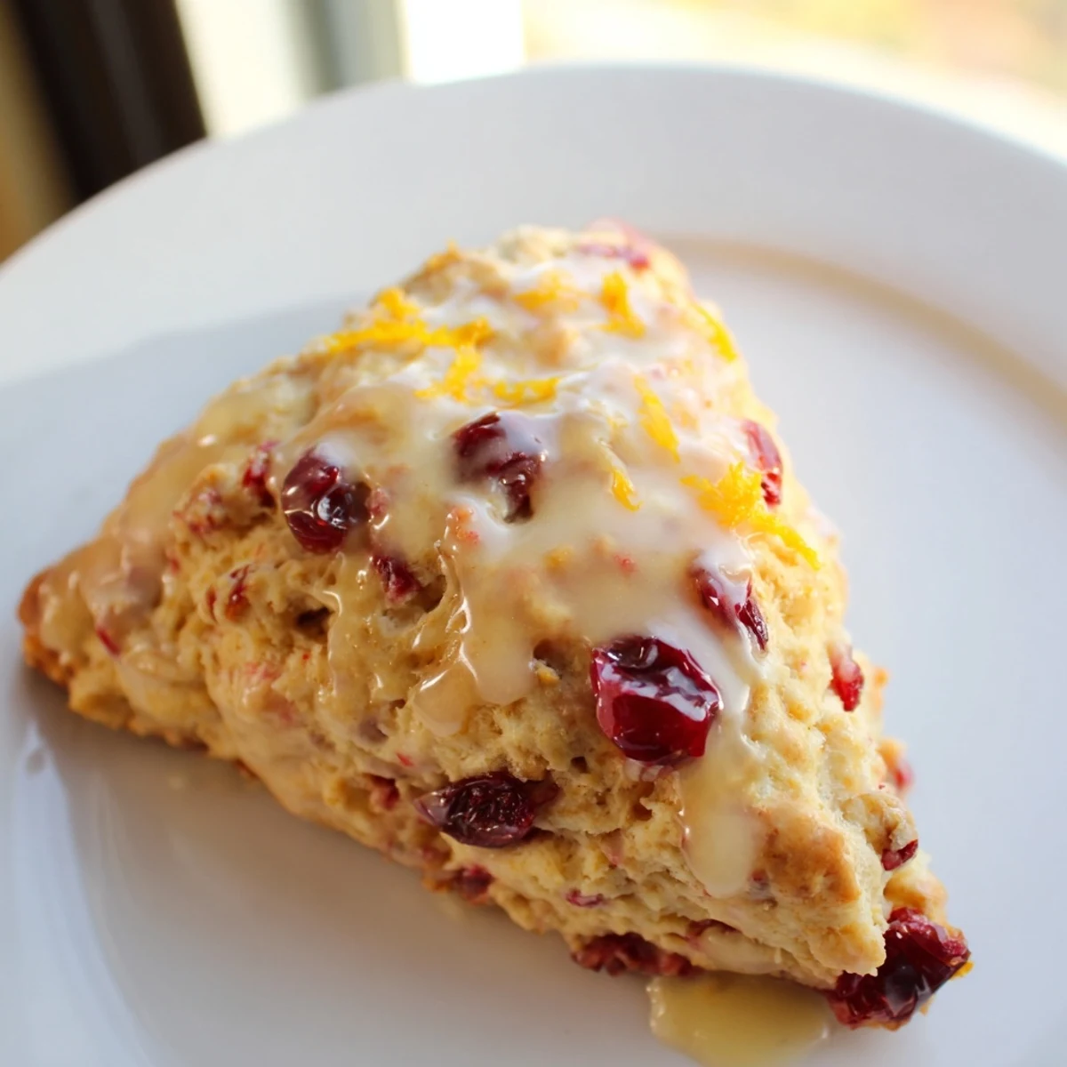 A close-up view of warm Cranberry Orange Scones with Orange Glaze, highlighting flaky layers and sugary citrus topping.