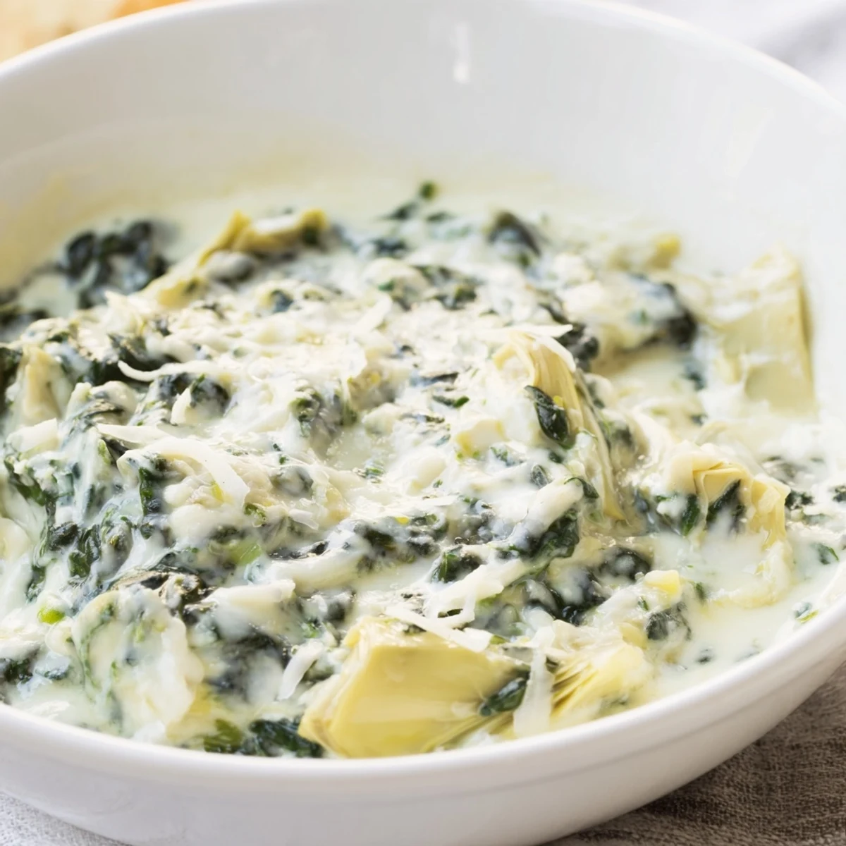 Creamy Spinach and Artichoke Dip in a white bowl, topped with melted mozzarella and ready for a party platter.