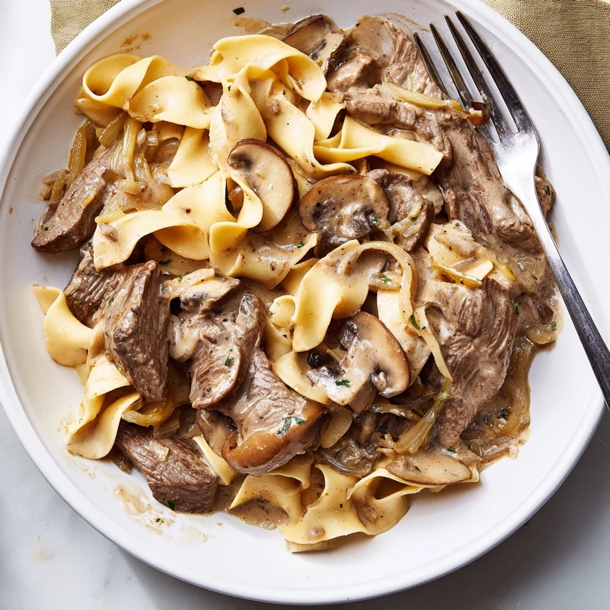 Warm Beef Stroganoff with Egg Noodles garnished with fresh parsley, served family-style beside a crisp green salad on a wooden table.