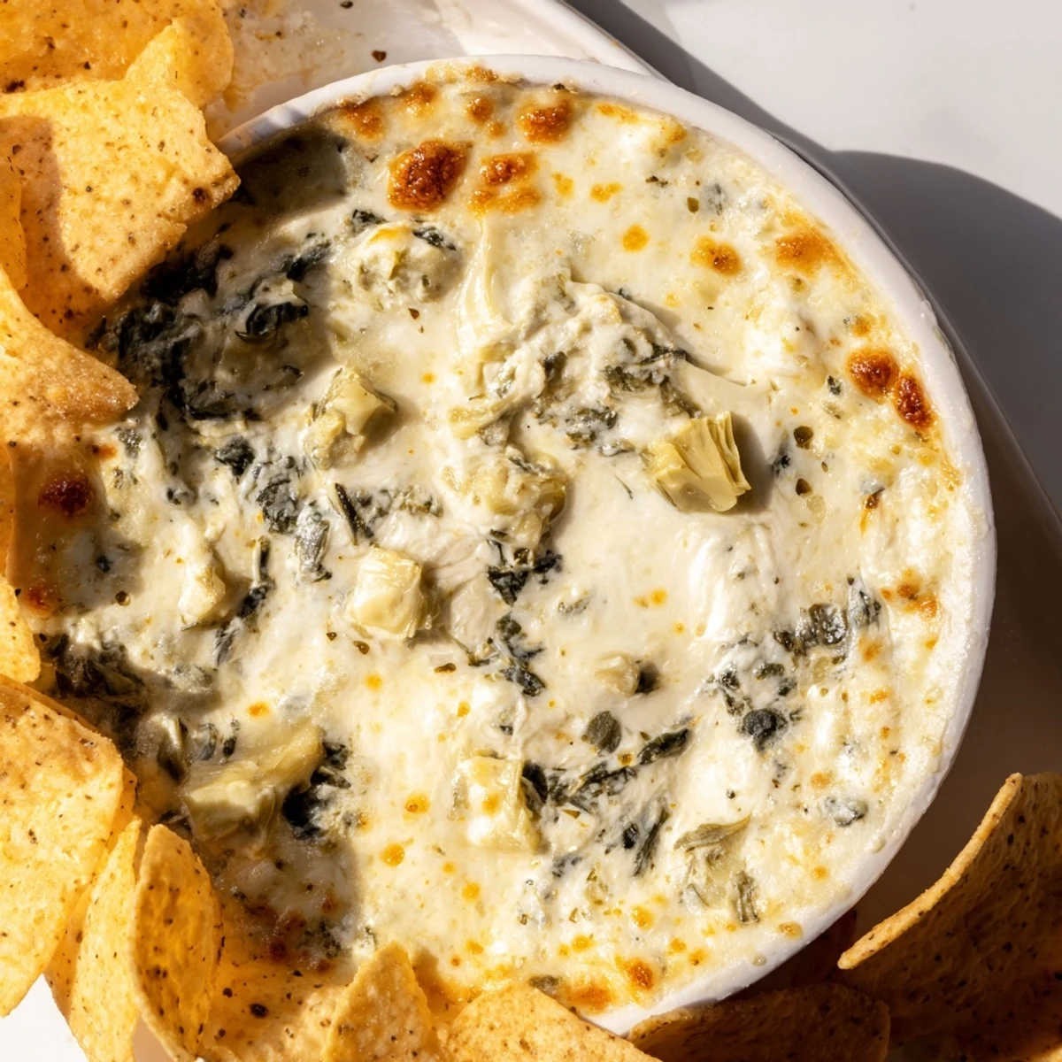 Close up of Creamy Spinach and Artichoke Dip with Chips showing melted mozzarella and Parmesan, paired with crispy golden chips.