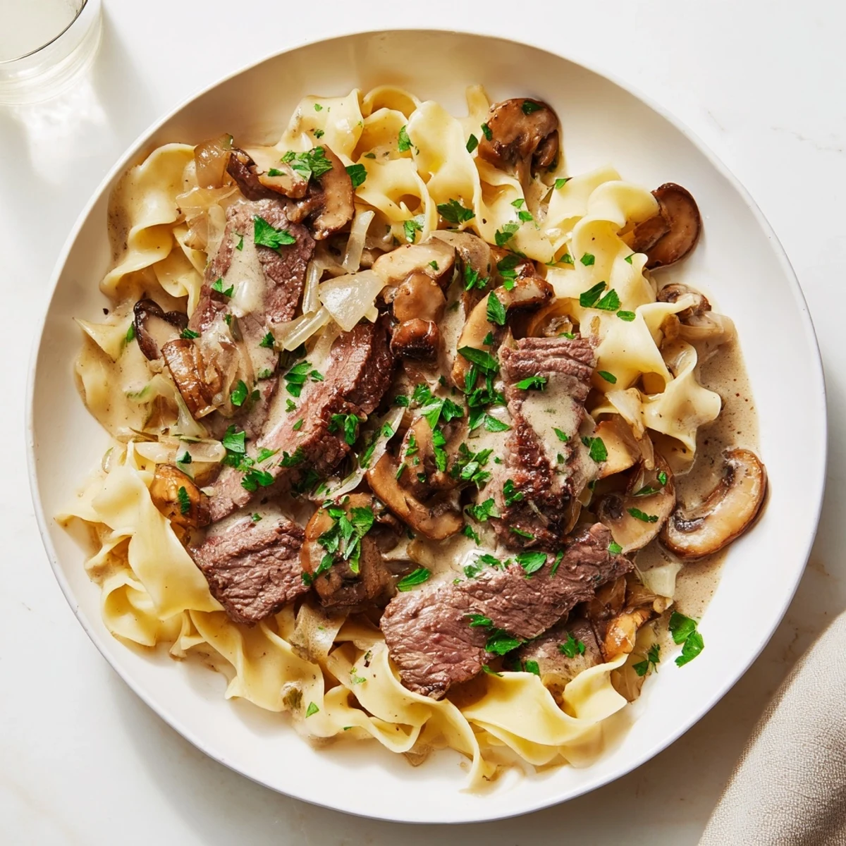 Steaming creamy beef stroganoff with egg noodles served in a white bowl, garnished with fresh parsley and a swirl of rich sauce.