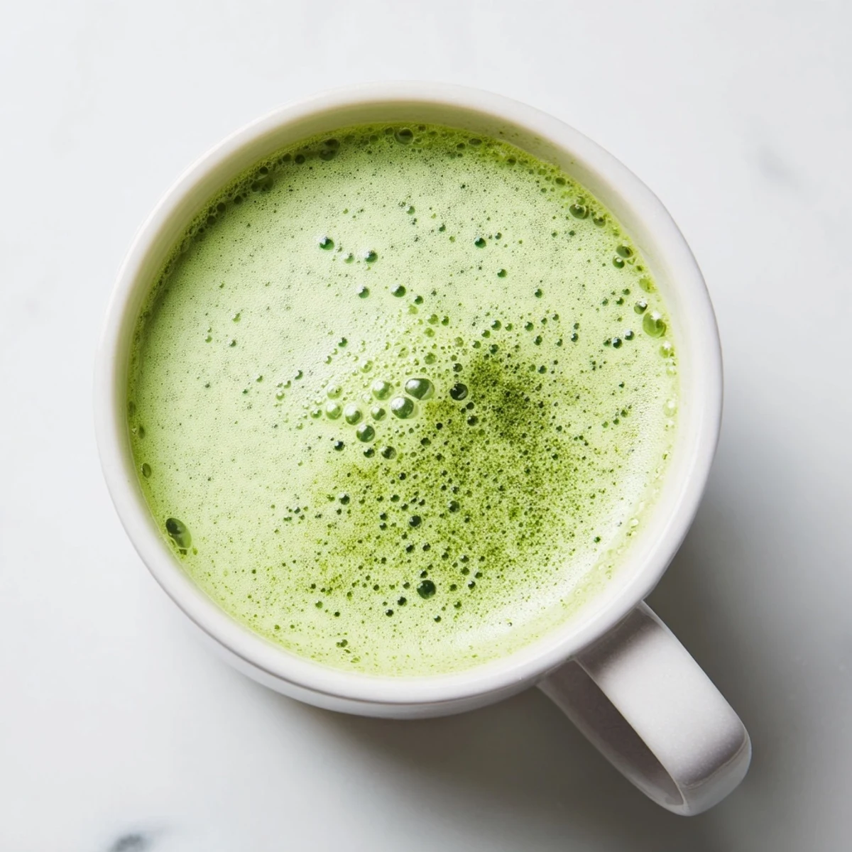 Close-up of vibrant green tea swirls in a creamy Green Matcha Latte with Almond Milk, topped with a light foam.  