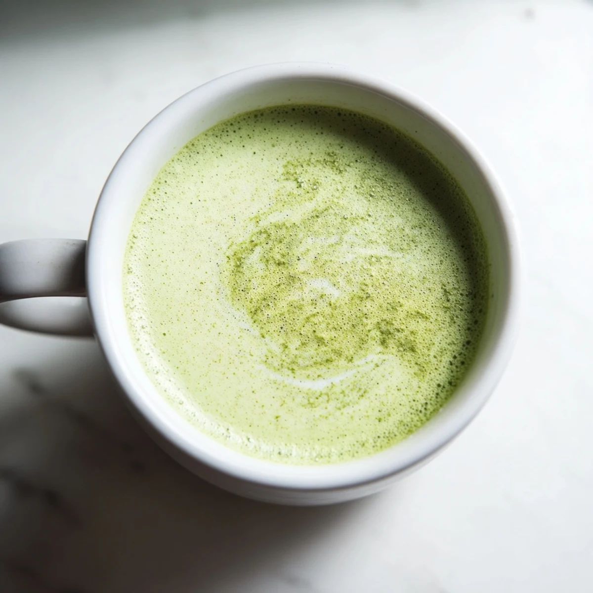 Vibrant green matcha latte with almond milk in a glass, topped with creamy foam for a refreshing sip.