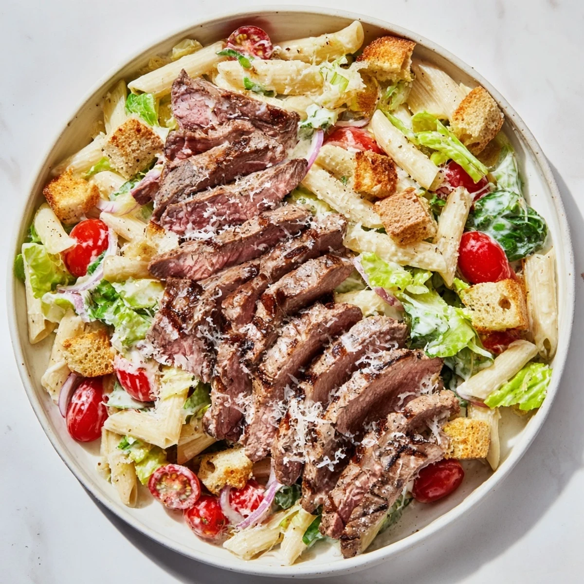 The Flavorful Steak Caesar Pasta Salad is served in a wooden bowl with croutons and shaved Parmesan for lunch.