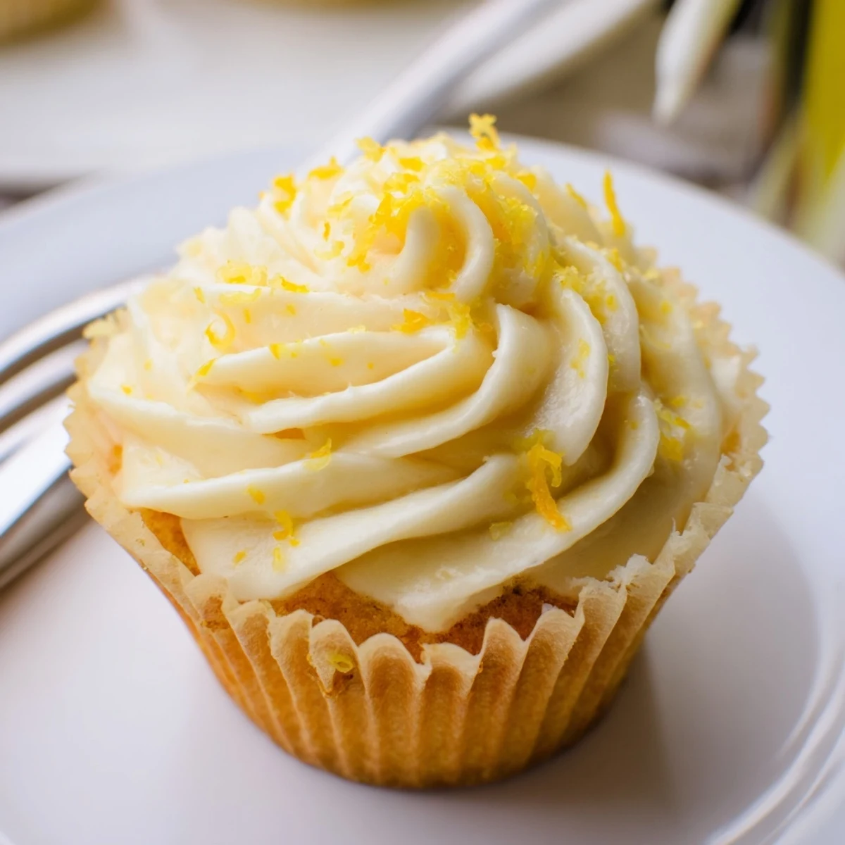 Limoncello cupcakes with bright yellow buttercream swirls, a plate of twelve garnished with lemon zest.