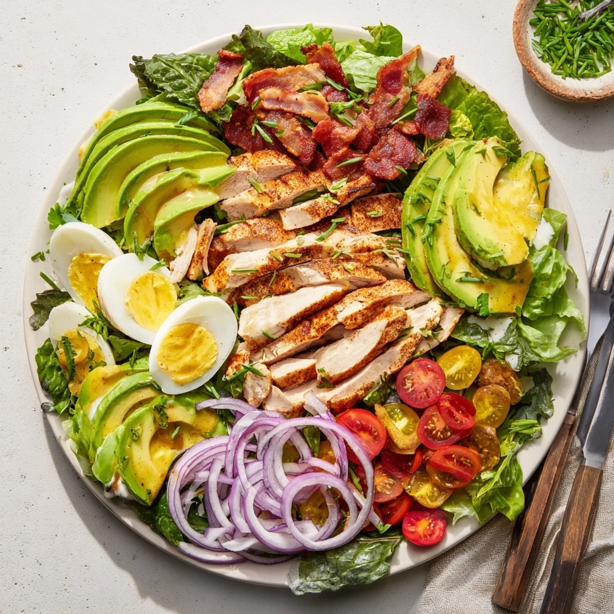 Vibrant Paleo Grilled Chicken Cobb Salad With Honey Dijon Dressing topped with sliced avocado, cherry tomatoes, and hard-boiled eggs.