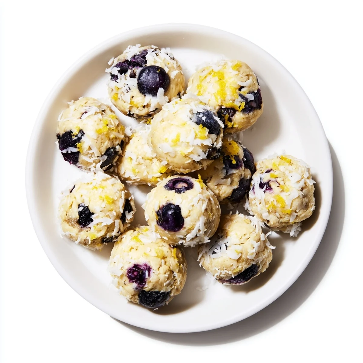 A close-up photo reveals the moist, chewy texture of Lemon Blueberry Cottage Cheese Protein Bites, with shredded coconut coating and a bright blueberry in every bite.