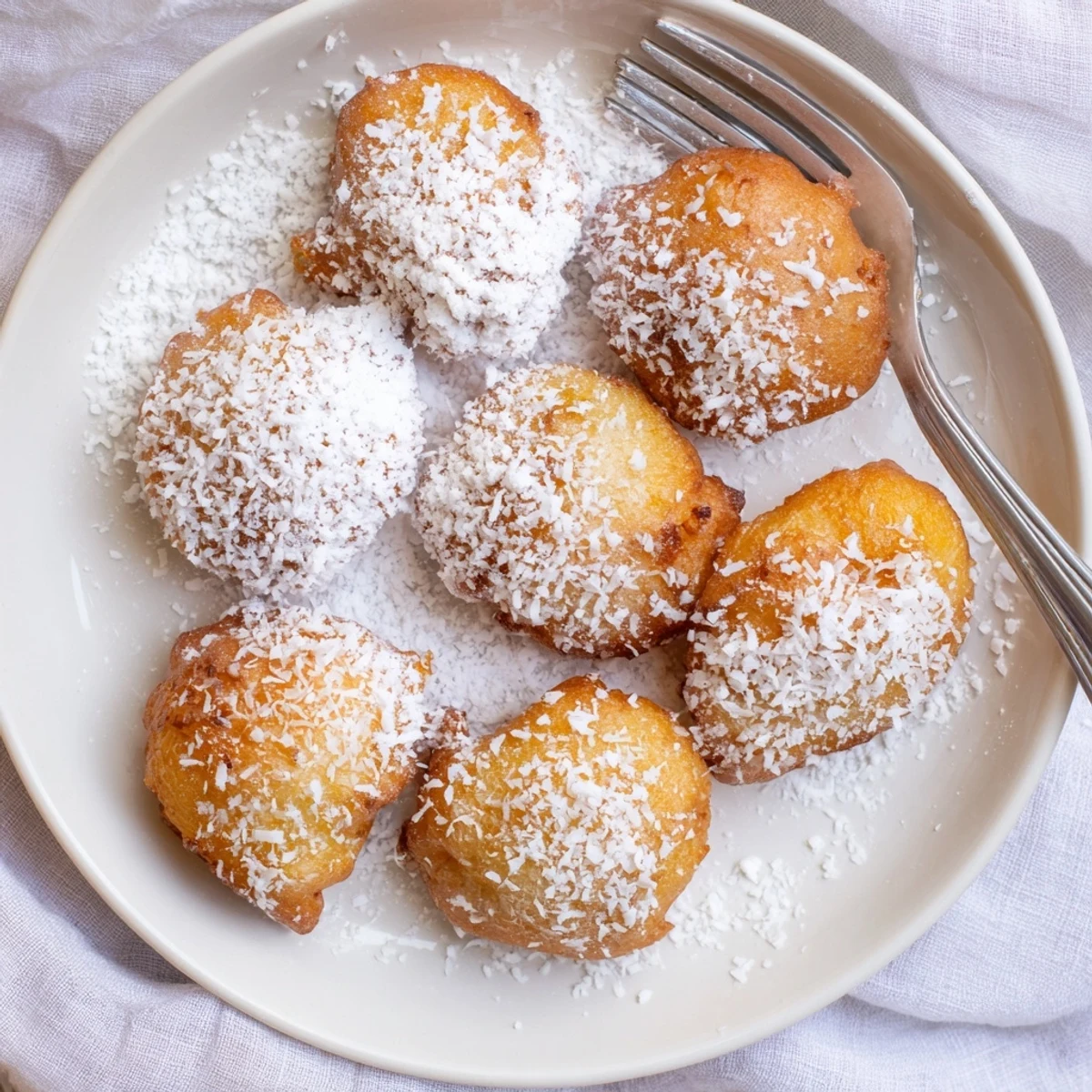 Golden pineapple fritters dusted with powdered sugar on a white serving plate