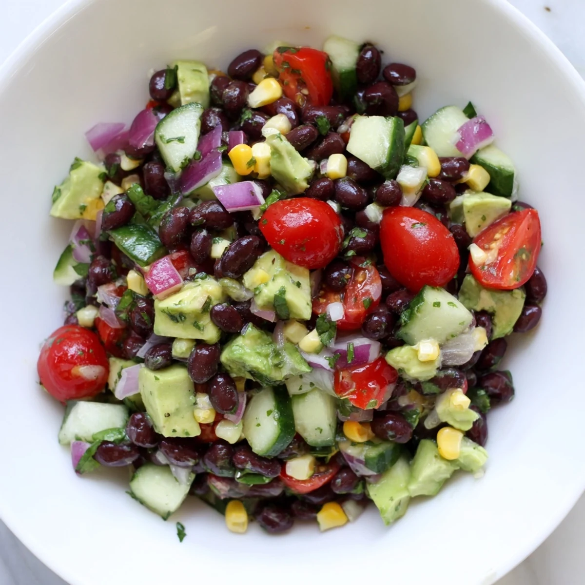Fresh chopped black bean salad with crisp cucumber, ripe avocado chunks, and red onion drizzled with olive oil lime dressing