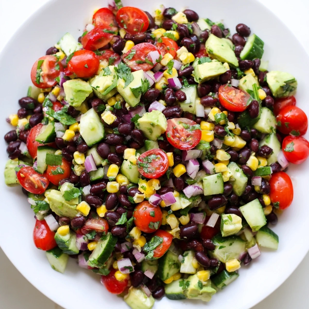 Colorful chopped black bean salad with fresh vegetables, creamy avocado, and zesty lime dressing in a white bowl
