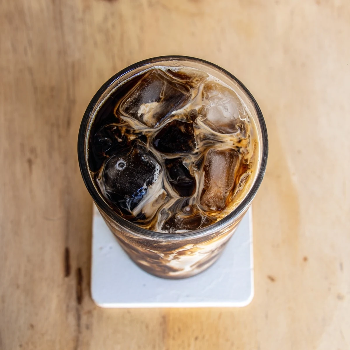 Cold refreshing iced coffee with milk swirling over ice cubes in a clear glass
