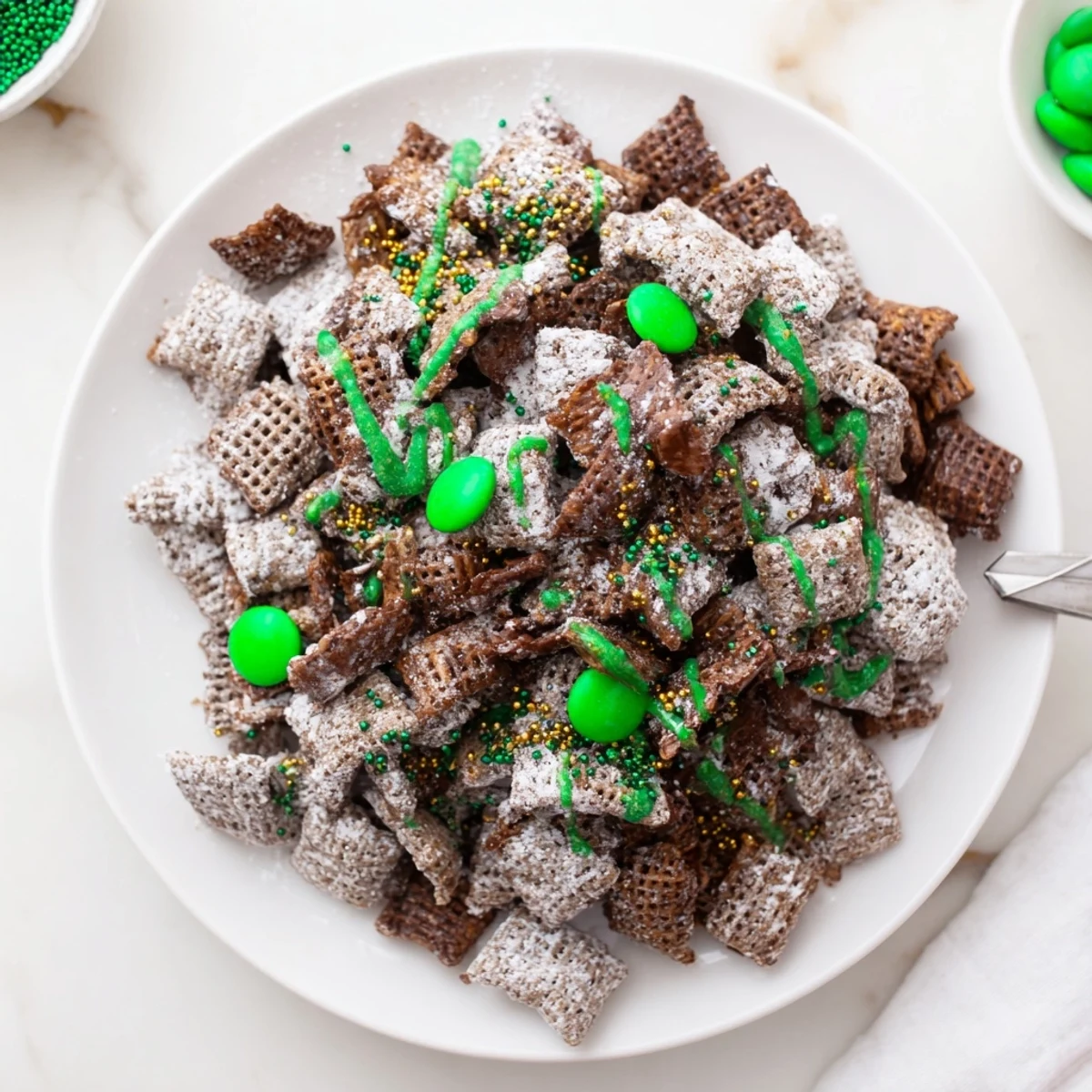 Festive green and white St. Patricks Day puppy chow coated in powdered sugar and green candy drizzle with gold sprinkles