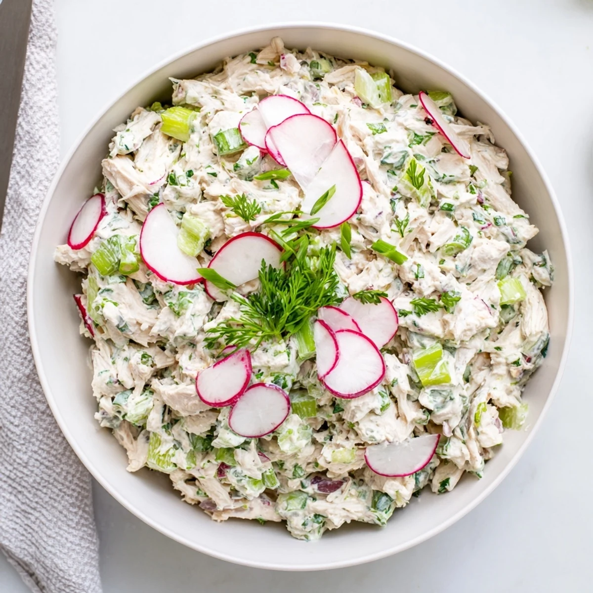 Vibrant green dip featuring shredded chicken and chopped herbs surrounded by sliced cucumbers and radishes