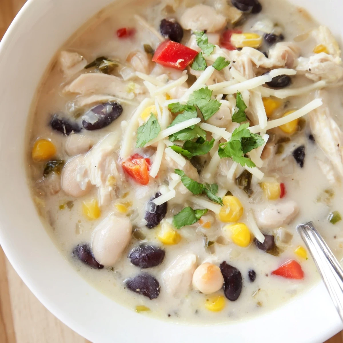 Creamy white chicken chili bowl topped with cheese, cilantro, and black beans in a rich, thick broth