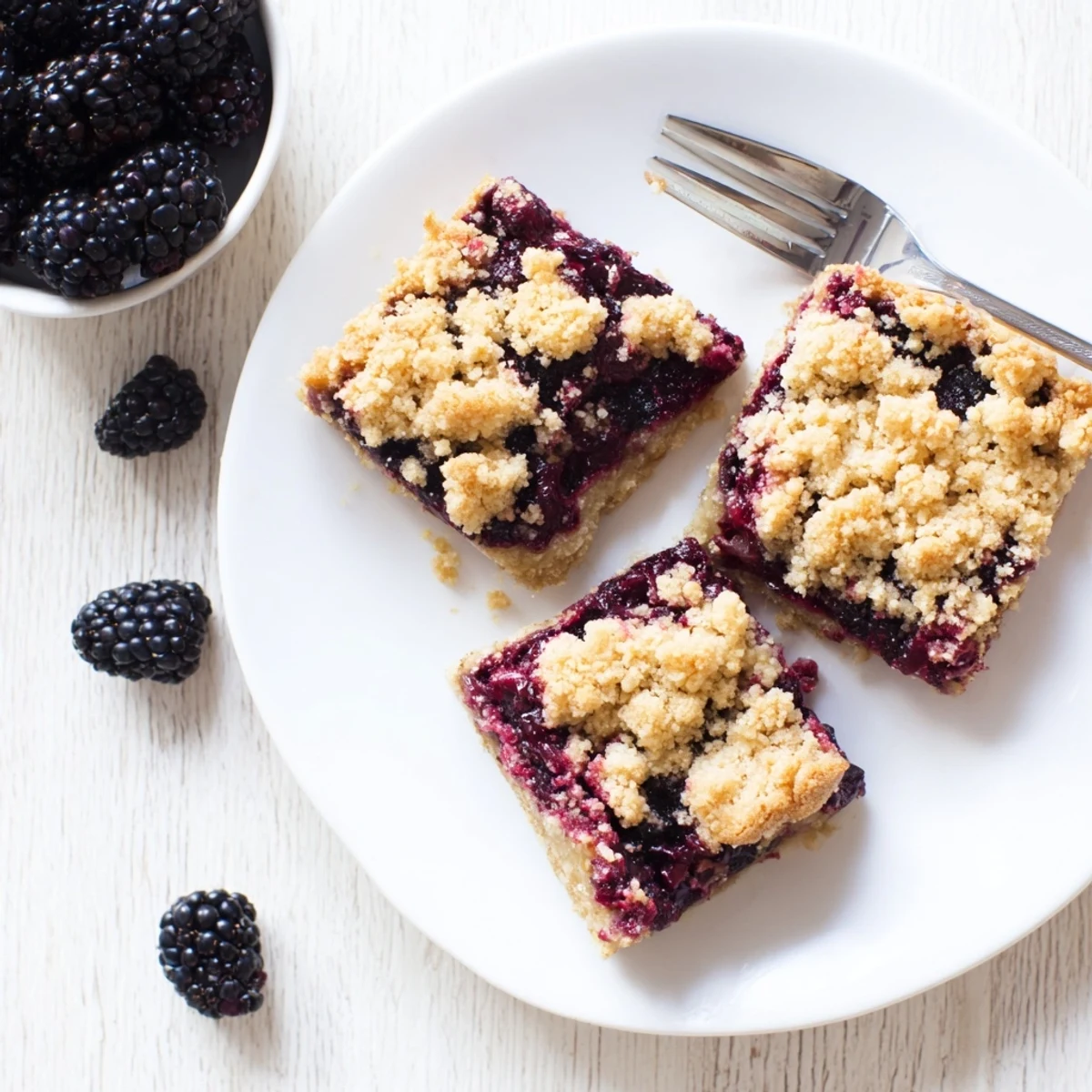 Golden blackberry crumble bars with bubbling fruit filling and buttery oat topping on a white plate