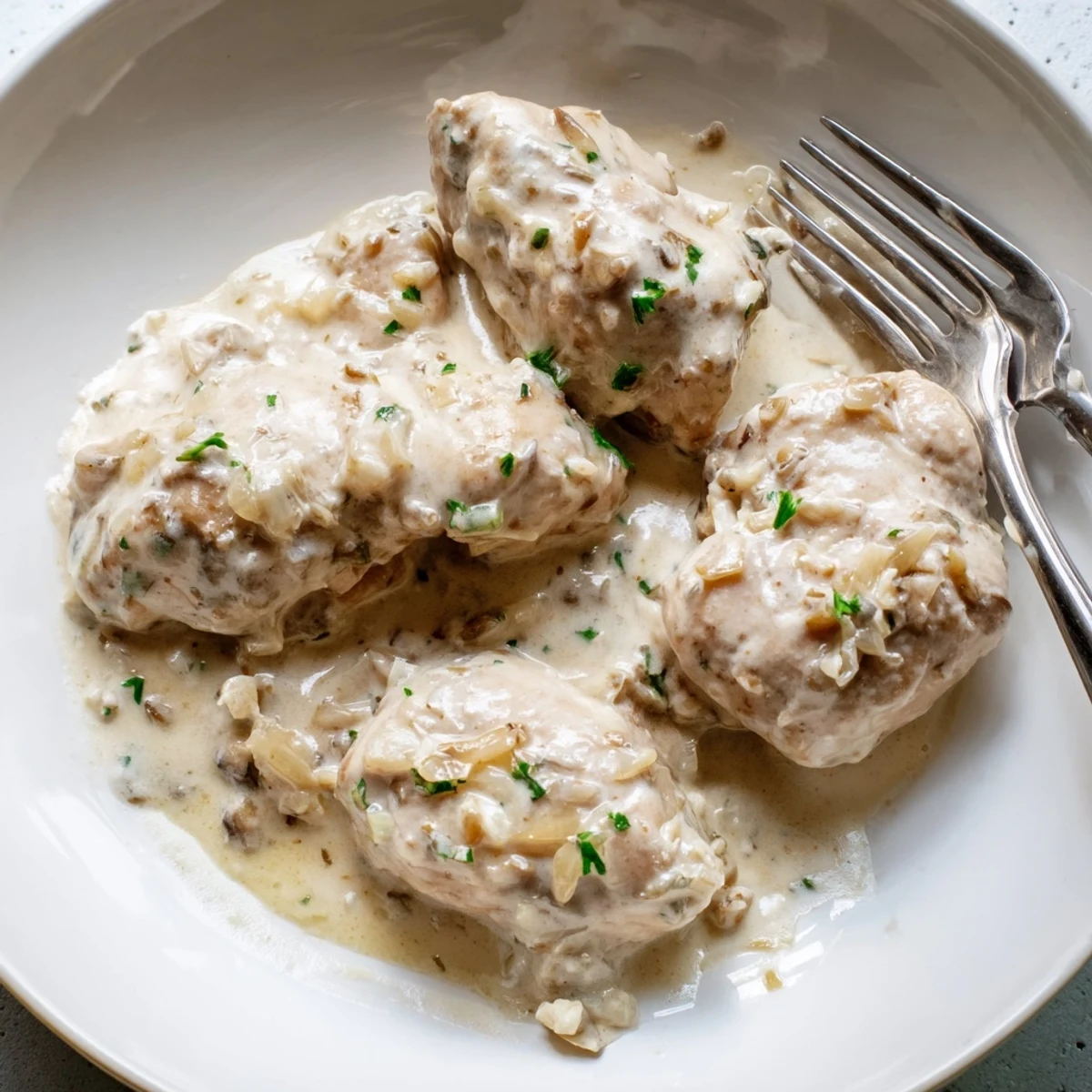 Succulent boneless chicken thighs plated with thick homemade gravy garnished with fresh Italian herbs.