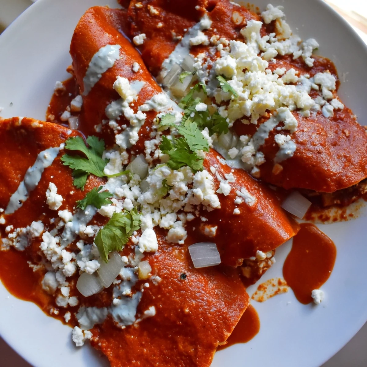 Warm entomatadas folded and smothered in vibrant red tomato salsa with creamy Mexican crema drizzle