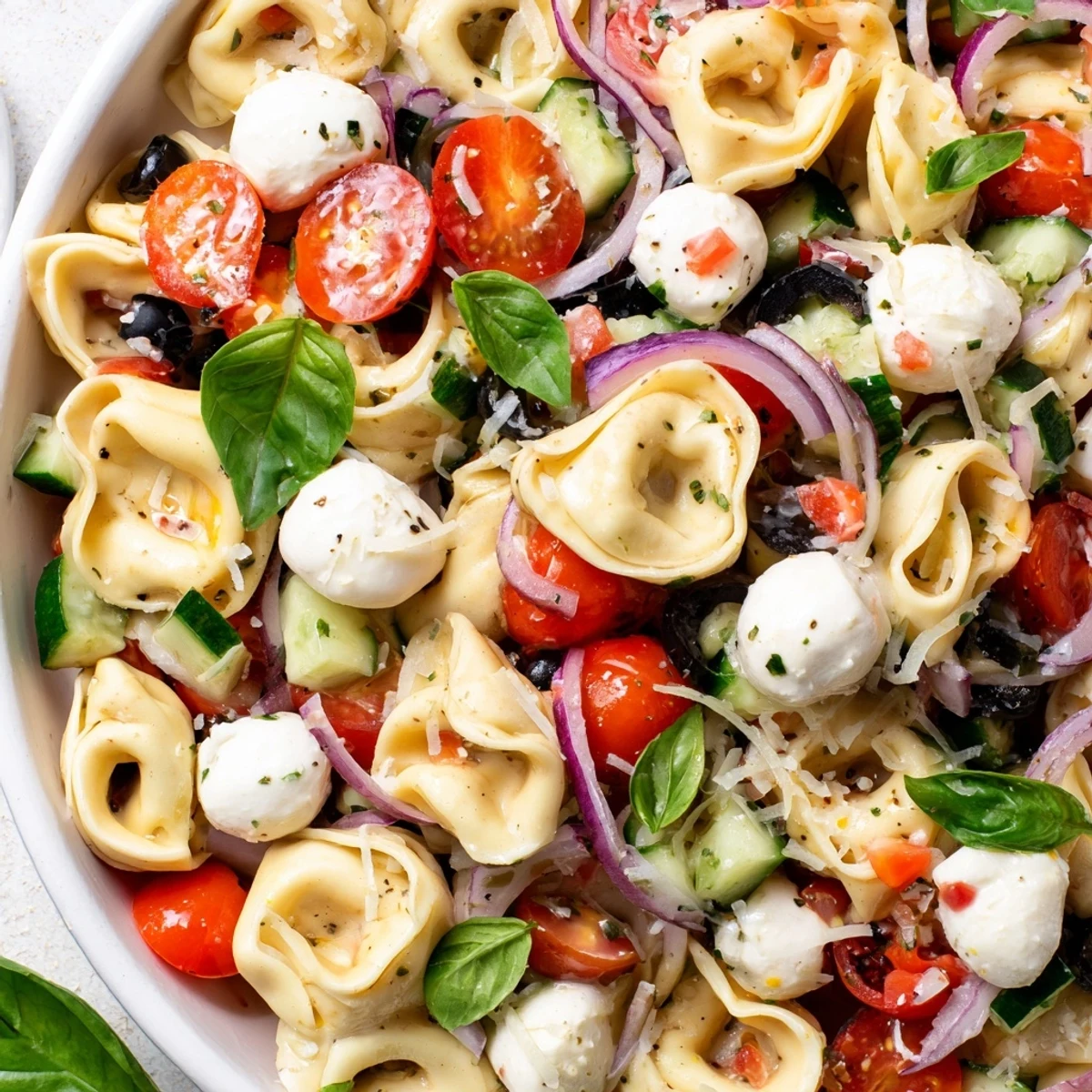 Creamy cheese tortellini salad garnished with fresh basil, olives, and vibrant diced vegetables