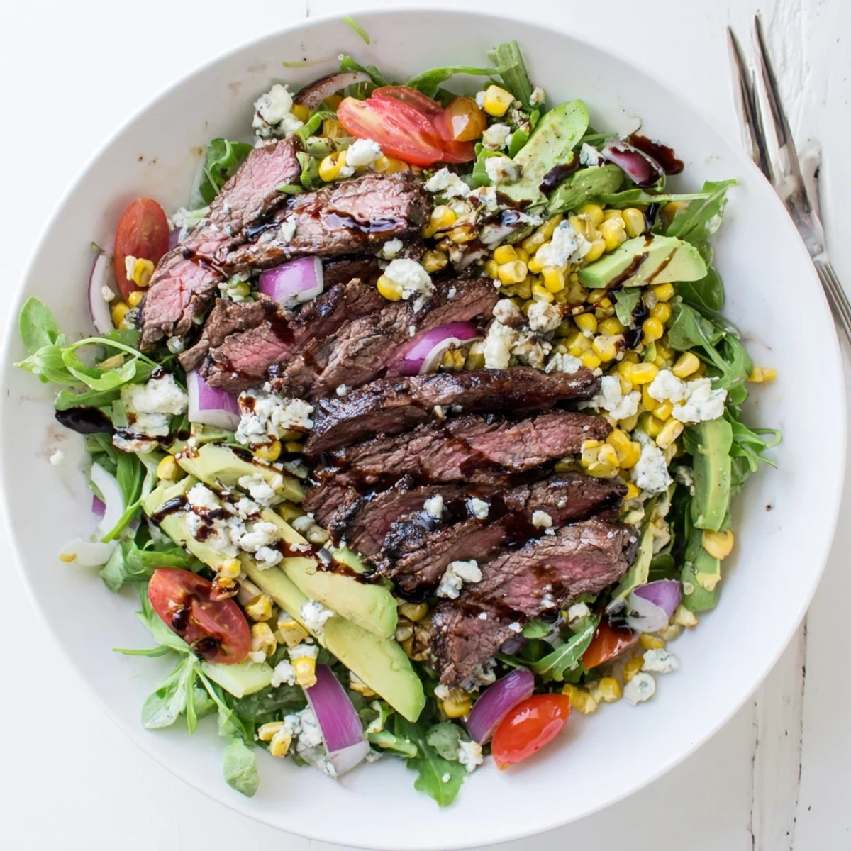 Sliced balsamic-marinated steak layered over crisp greens in a balsamic steak Gorgonzola salad with grilled corn