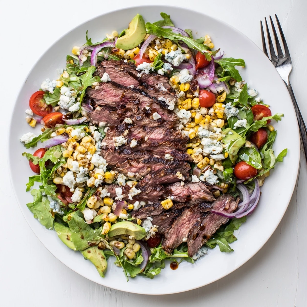 A hearty balsamic steak Gorgonzola salad with grilled corn plated on a wide white serving dish