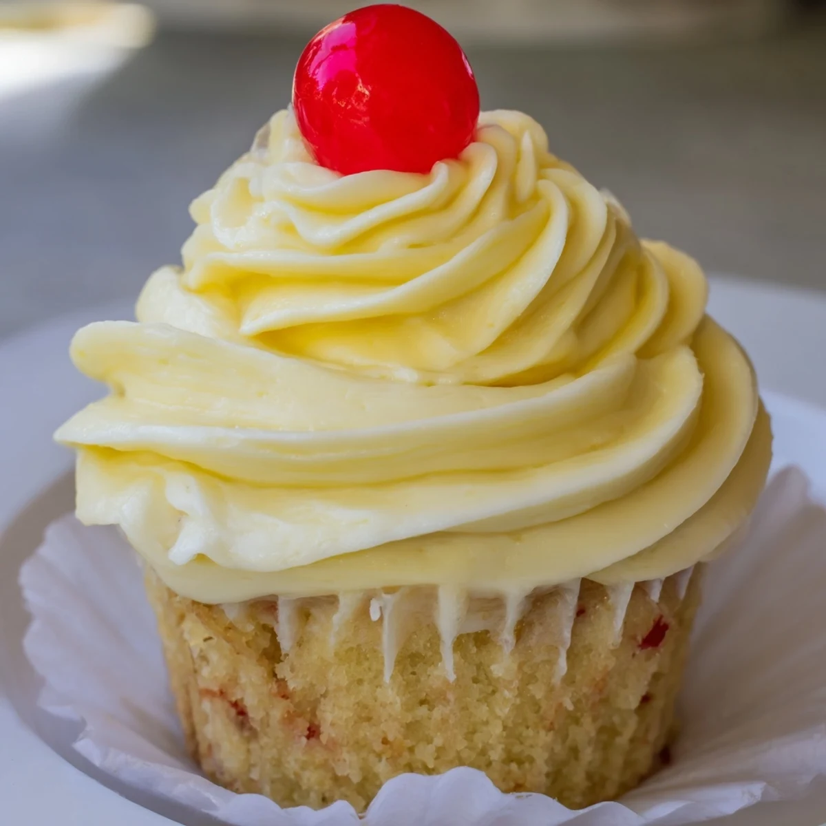 Moist pineapple-infused Dole Whip Cupcakes piped with creamy yellow frosting on a white plate