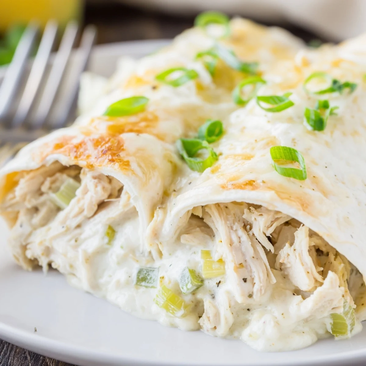 Creamy White Chicken Enchiladas bubbling golden in baking dish, cilantro and scallions