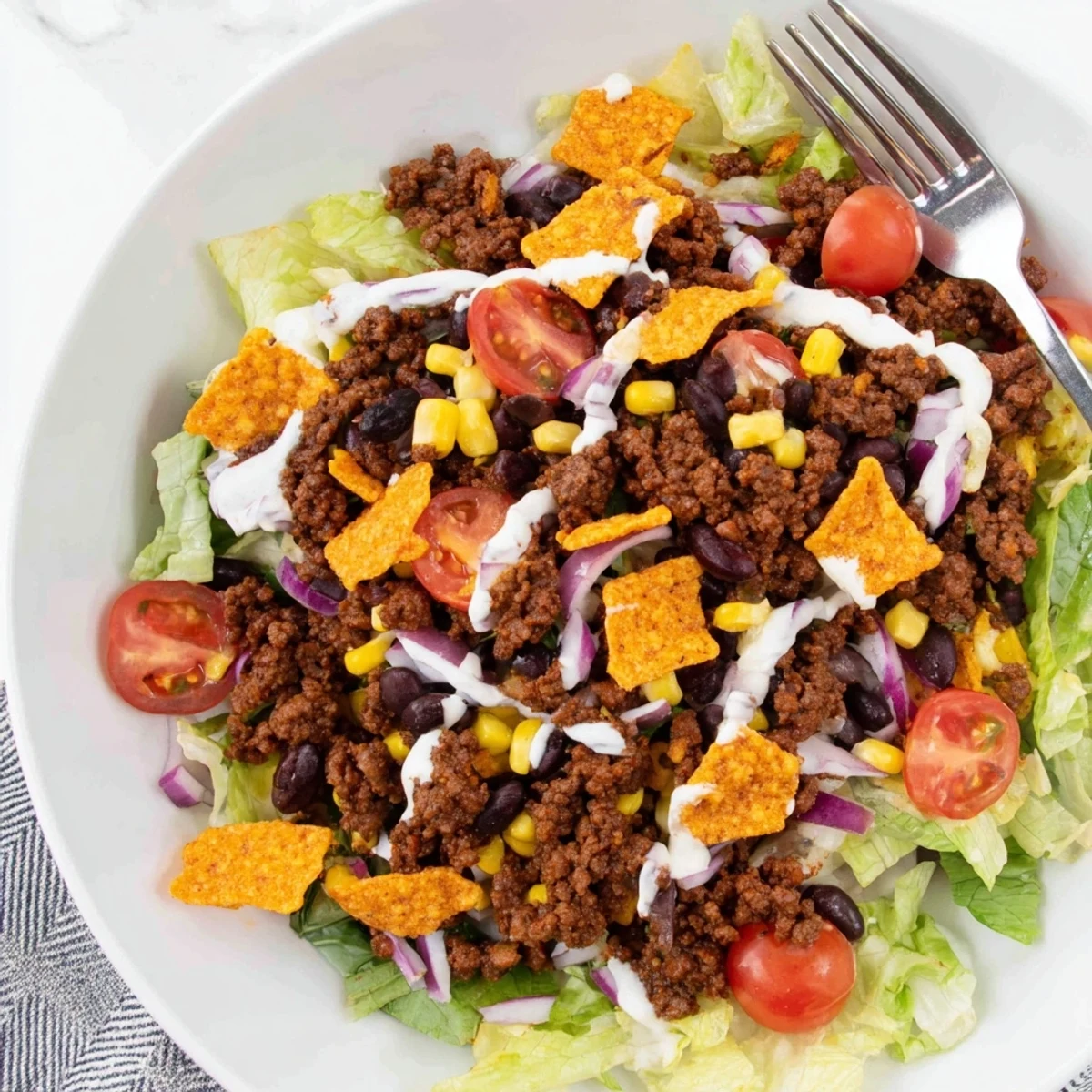 A bowl of Simple Doritos Taco Salad topped with shredded cheddar and ranch