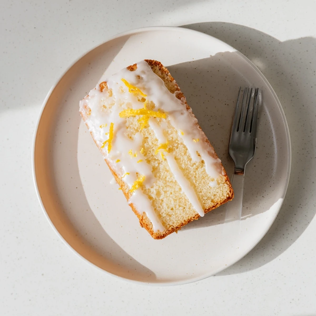 Golden Greek yogurt lemon loaf drizzled with white glaze on a wooden cutting board