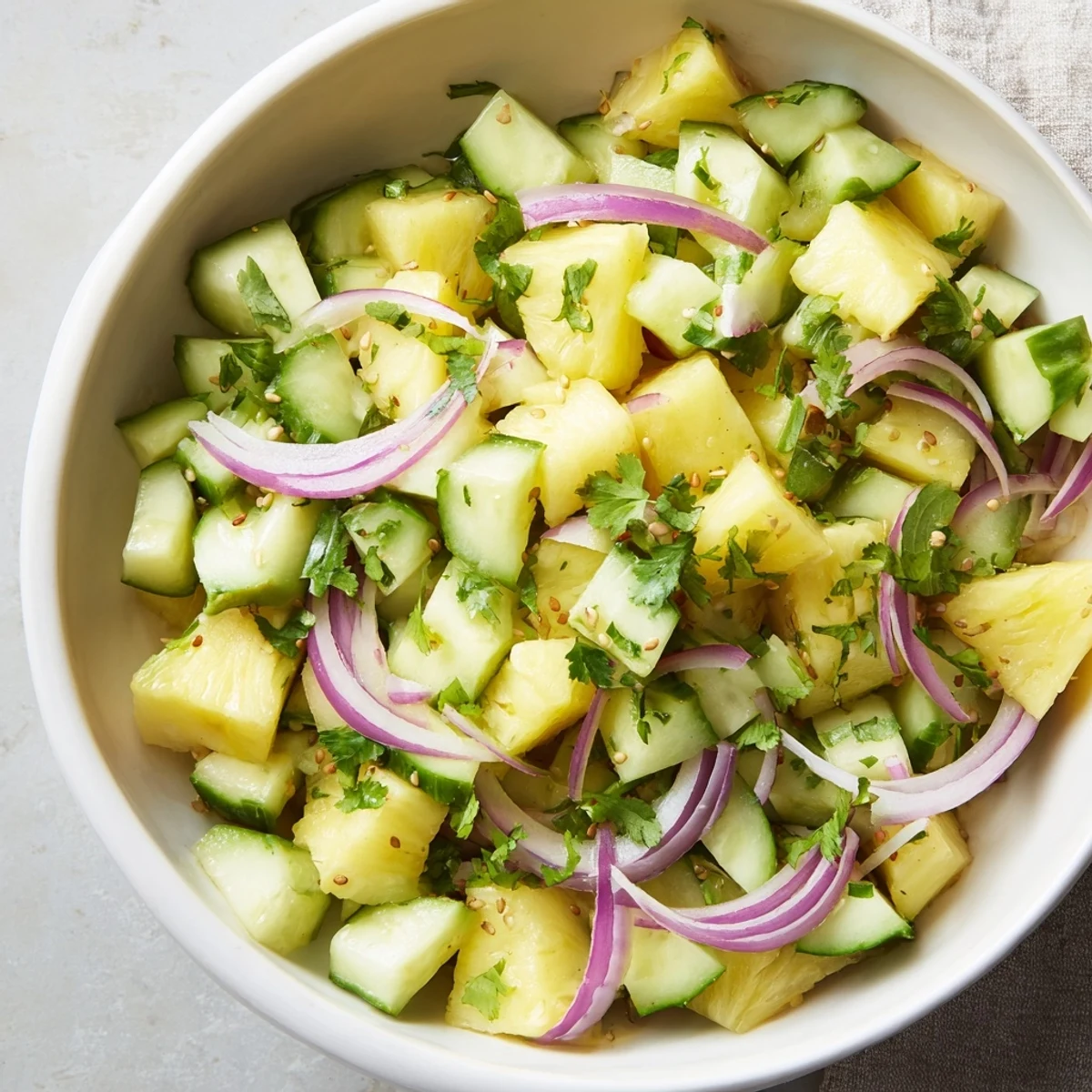 Colorful bowl of diced pineapple and cucumber salad garnished with fresh cilantro and toasted sesame seeds