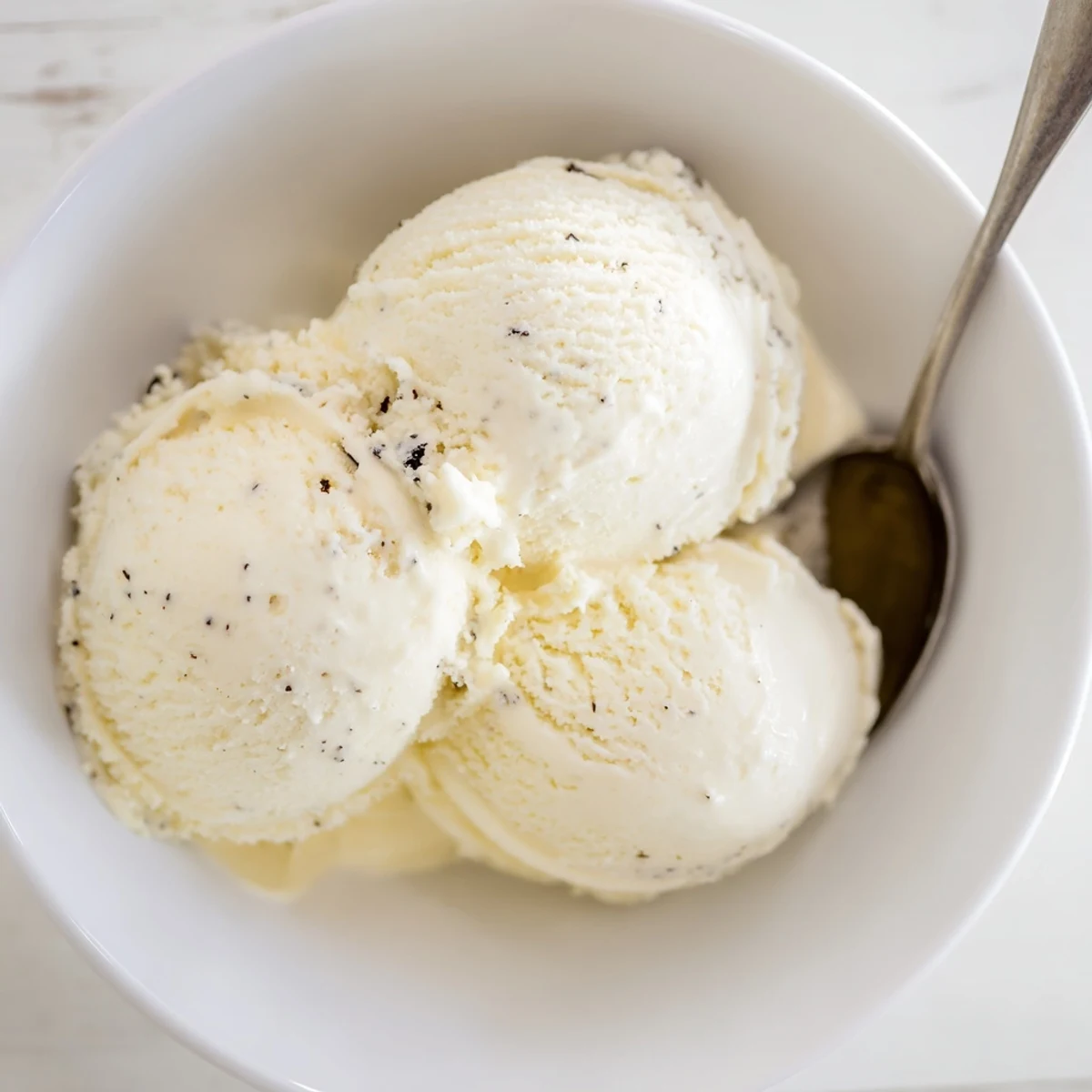 Silky smooth vanilla bean ice cream garnished with mint leaf and wafer cookie on wooden board