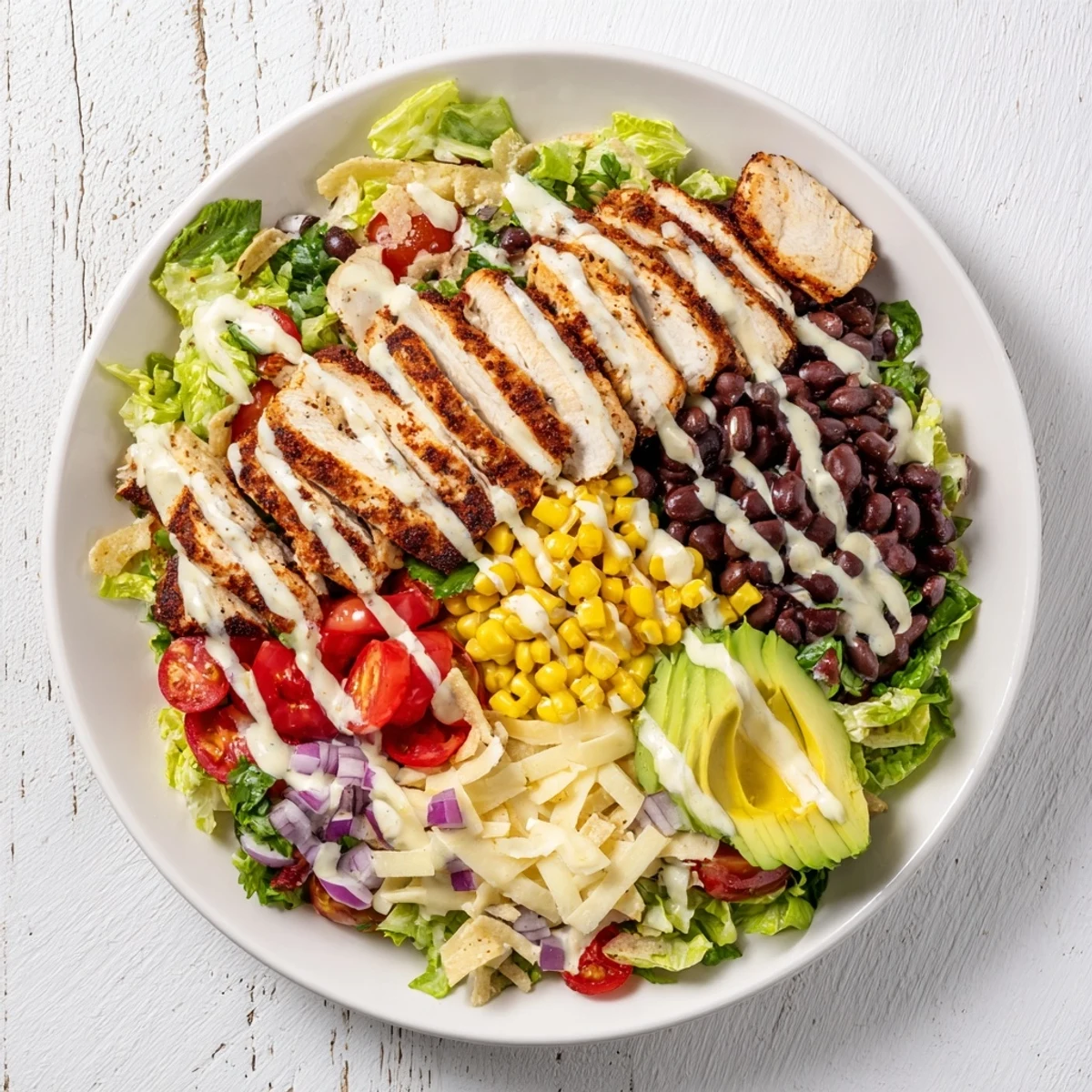 Colorful Southwestern chicken salad bowl with grilled sliced chicken, black beans, corn, avocado, and crisp vegetables drizzled with zesty lime dressing
