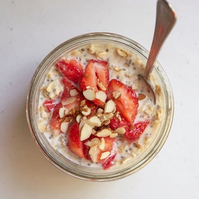 A spoon stirs the thick, honey-sweetened Strawberry Overnight Oats topped with sliced almonds. 