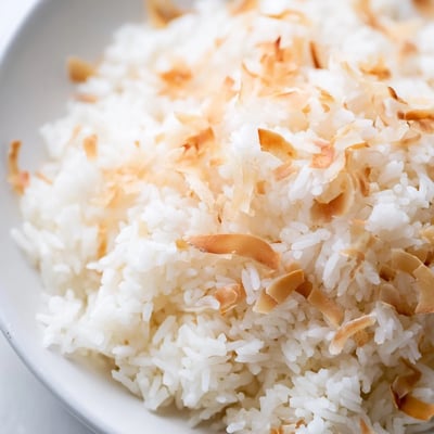 The Best Coconut Rice sits in a white bowl, fragrant with jasmine rice and coconut milk, paired with vibrant curry.
