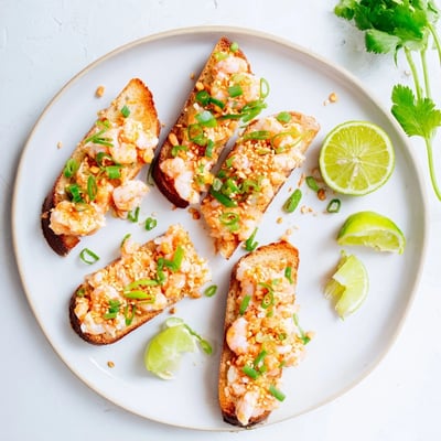 Crispy baguette slices holding a vibrant mix of Cajun shrimp, scallions, and sesame seeds for an appetizer.