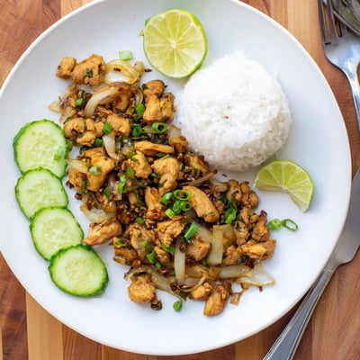 Steamed jasmine rice and cucumber slices alongside vibrant Vietnamese Lemongrass Chicken on a white plate.