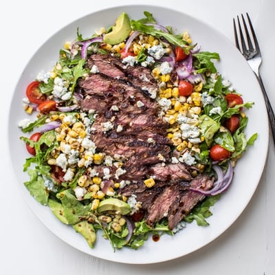 A hearty balsamic steak Gorgonzola salad with grilled corn plated on a wide white serving dish