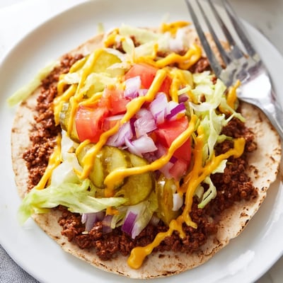 Golden flour tortillas cradling thin smashed beef patties topped with diced tomato and pickles